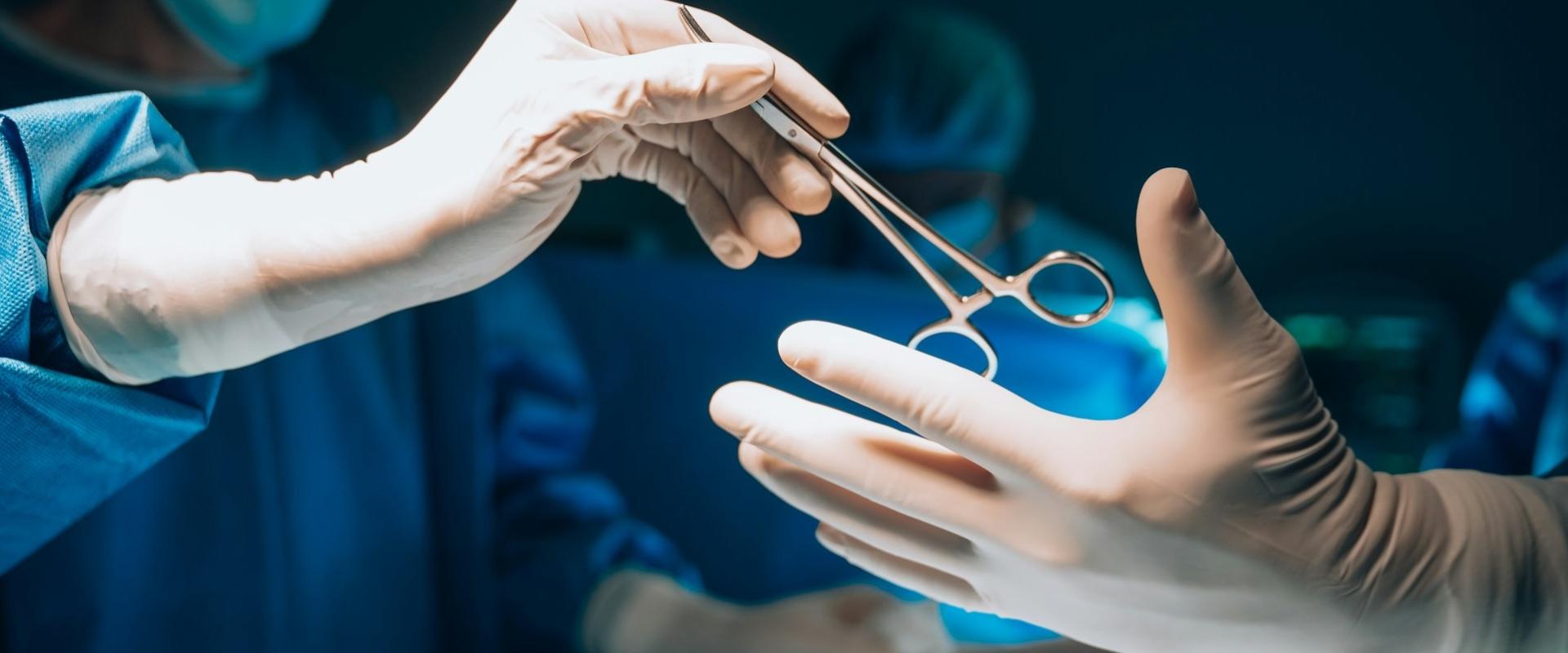 Gloved hands of medical professionals passing surgical scissors during an operation, with one hand handing the instrument to another outstretched hand